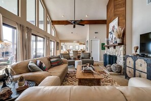 A spacious living area with a large sofa, a coffee table, and a stone fireplace. There is a television on a wooden cabinet and a ceiling fan. - Waterfront PK Lake Home with Private Boat Dock (Graford)