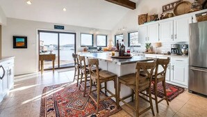 Une cuisine spacieuse dotée d’un grand îlot central, de meubles blancs et offrant une vue sur l’extérieur.