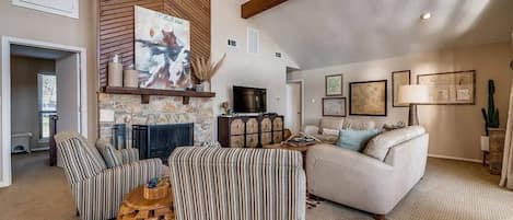 A spacious living room with a fireplace, striped armchairs, a sofa, and a ceiling fan.
