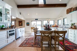 A spacious kitchen with white cabinetry, a central island with chairs, and a large window providing natural light. - Waterfront PK Lake Home with Private Boat Dock (Graford)