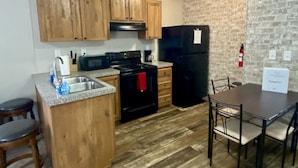A kitchen with wooden cabinets, a black refrigerator, a microwave, and a stove. There is a dining table with chairs and a bar stool. - Rainbow River Bungalow F (Dunnellon)