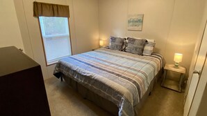 A bedroom with a bed, a window with blinds, a bedside lamp, and a wall-mounted picture. - Rainbow River Bungalow F (Dunnellon)