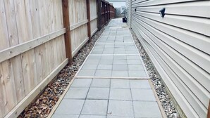 A narrow pathway flanked by wooden fences and a building with siding. - Luxury Suite • Private Yard • Hot Tub • King Bed (Sioux Falls)