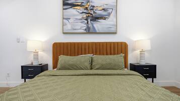 Un letto rifatto con cura, con una coperta a motivi verdi, affiancato da due comodini con lampade, e un quadro astratto moderno sopra il letto.