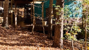 A rustic cabin with a covered porch and a small outdoor seating area, surrounded by a forest with autumn foliage. - Three-story Blue Ridge Yurt getaway (Pilot)