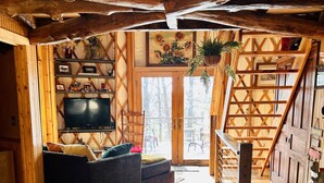 A cozy wooden interior with a sofa, television, and a staircase leading to an upper level. - Three-story Blue Ridge Yurt getaway (Pilot)