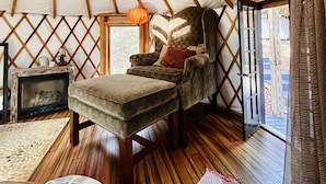 A cozy room with a wooden ceiling, a plush armchair, a small table, and a window. - Three-story Blue Ridge Yurt getaway (Pilot)