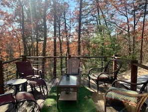 An outdoor deck with wooden furniture, including chairs and a table, surrounded by trees with autumn foliage.
