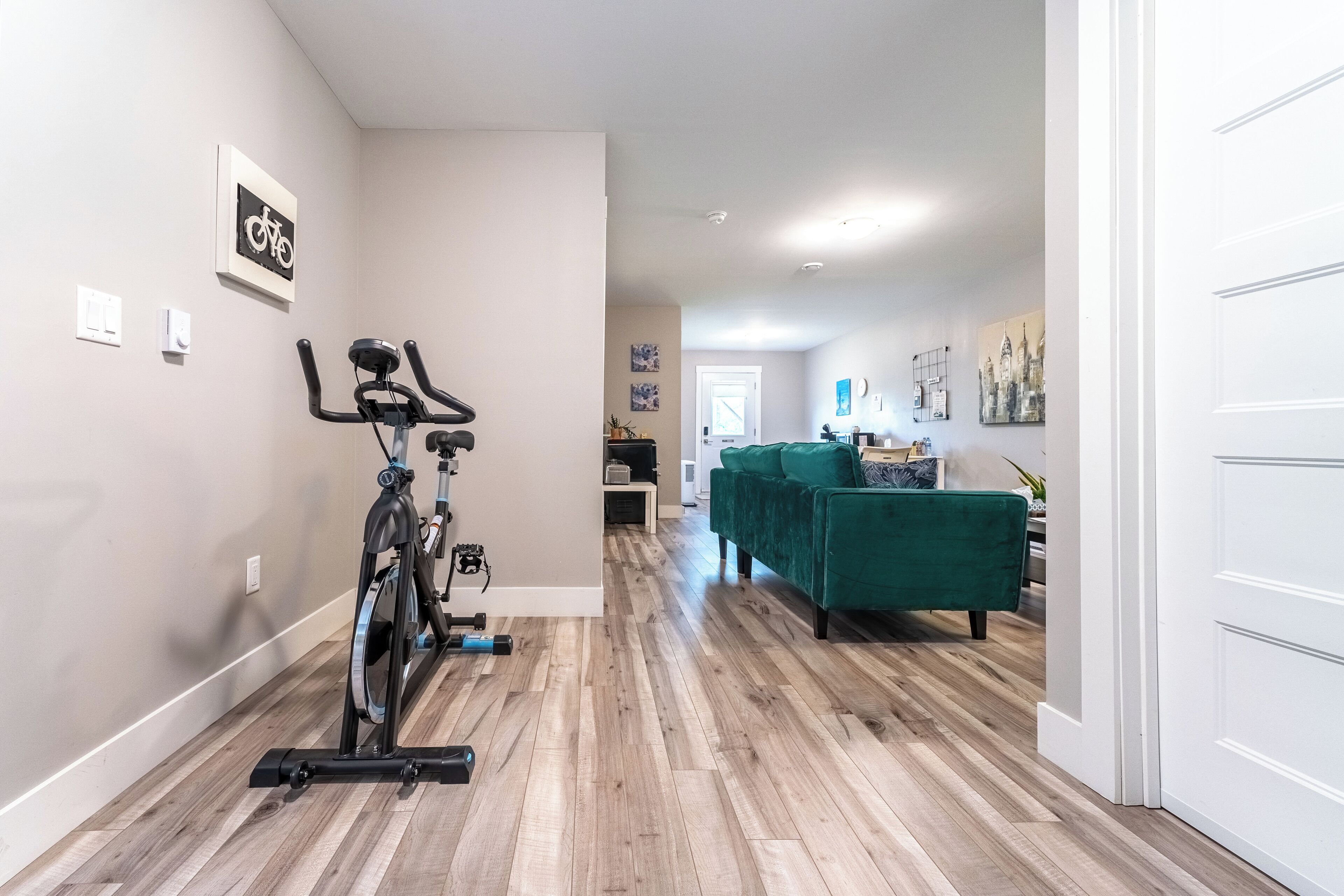 A spacious living area with a wooden floor, a green sofa, and a stationary bike.