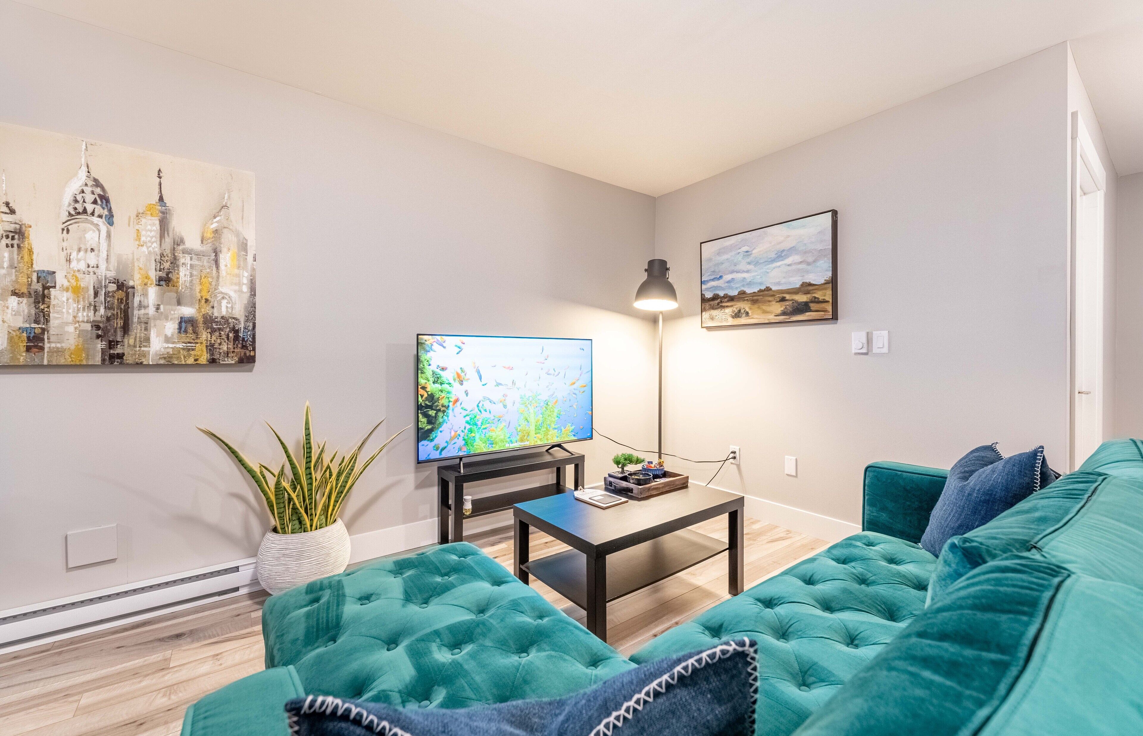 A modern living room with a teal sofa, a flat-screen TV, a floor lamp, and artwork on the walls.