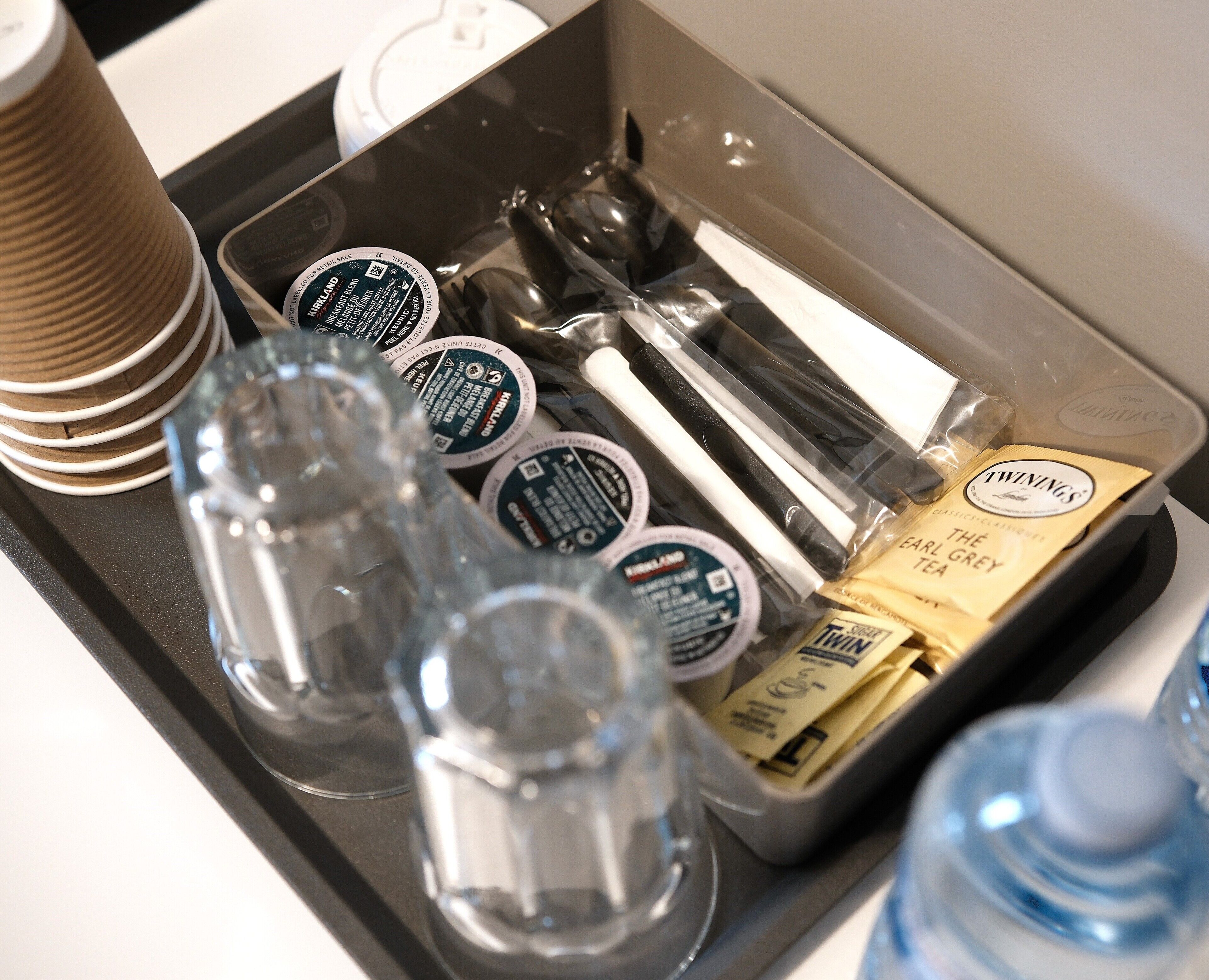 Ein Tablett mit einer Kaffeetasse, Teebeuteln, einer Wasserflasche und einem Glas.