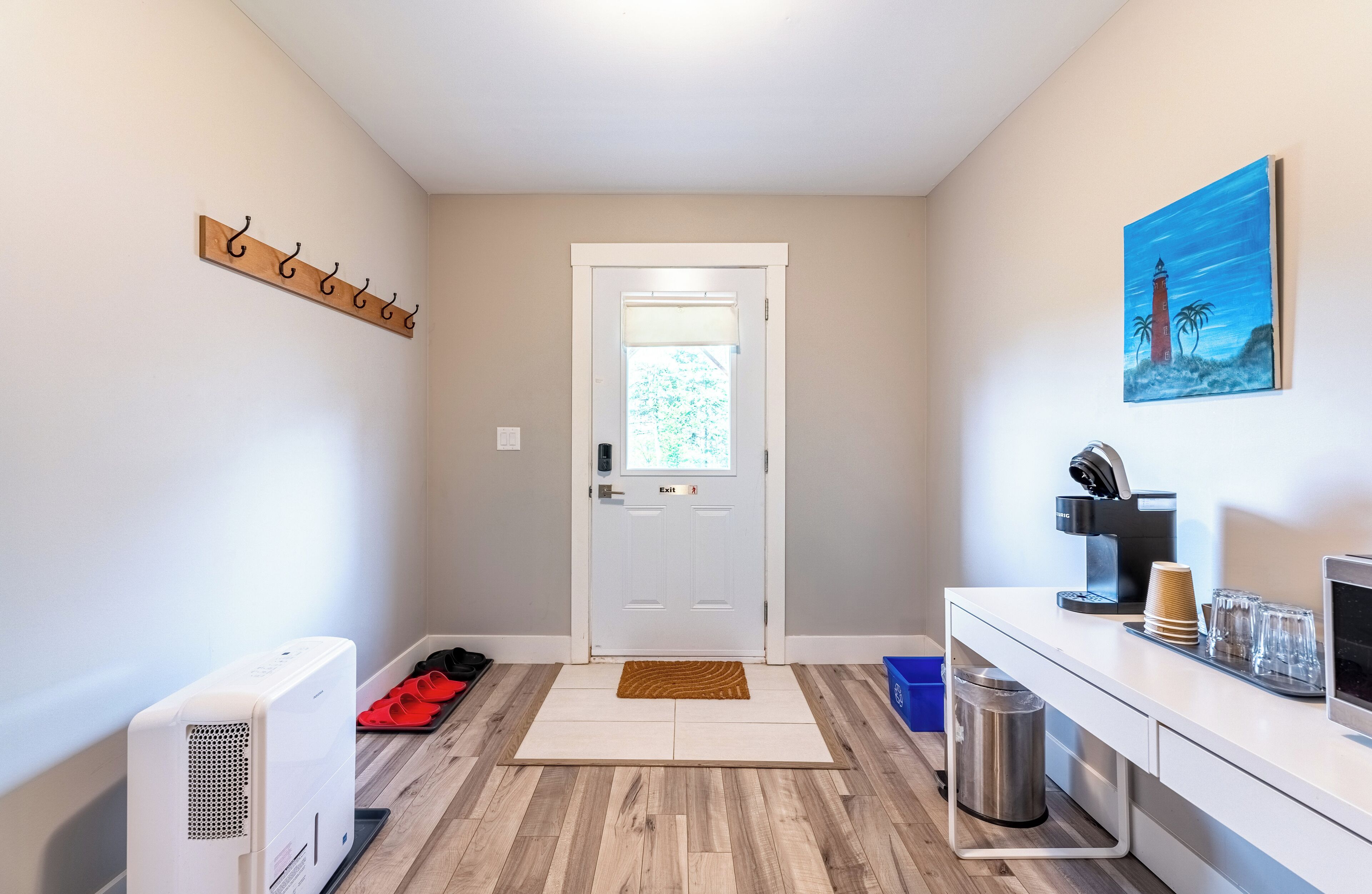 A hallway with a coat rack, a door, a coffee station, and a trash can.