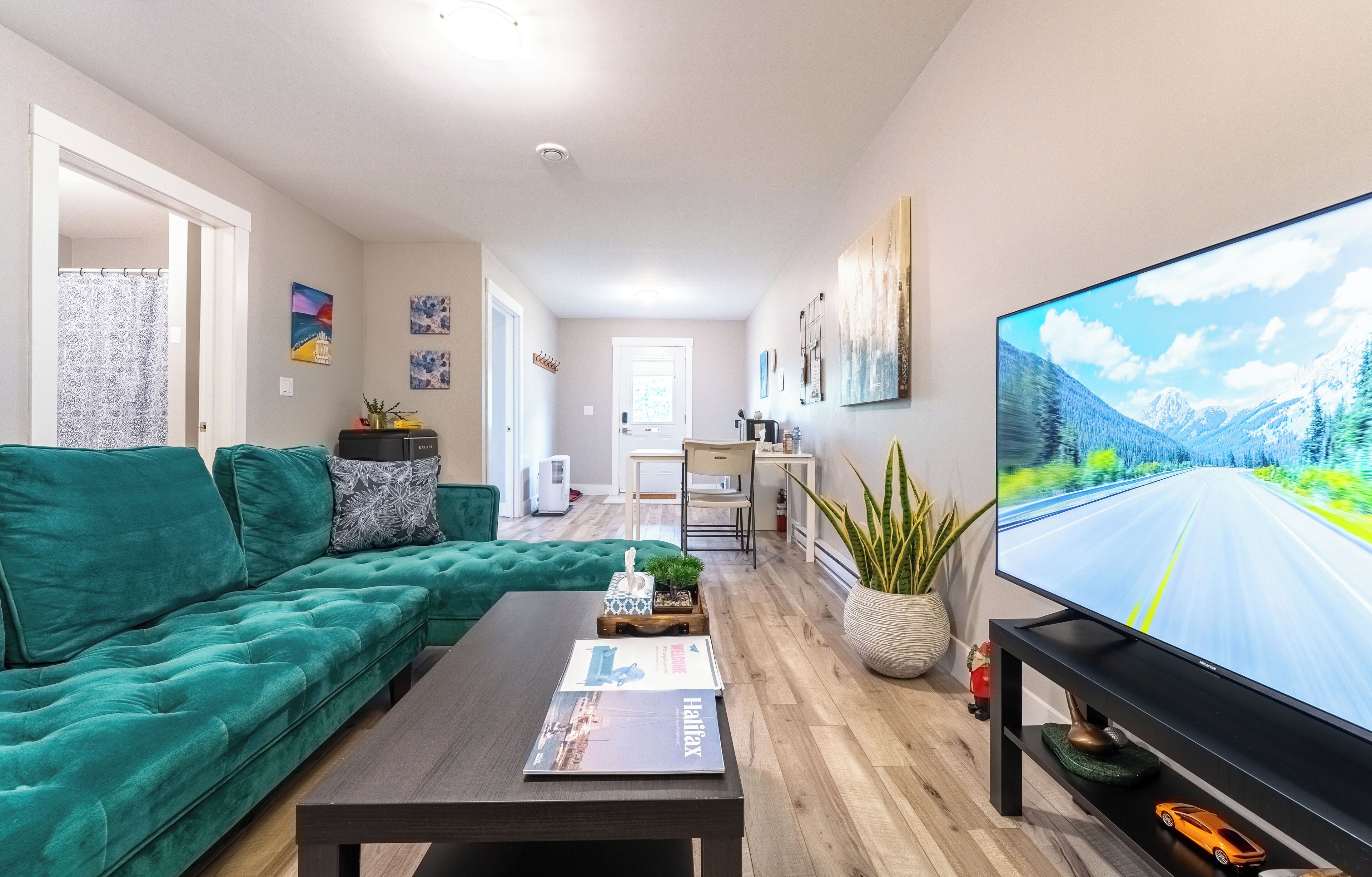 Una sala de estar moderna con un sofá verde, una mesa de centro y un televisor de pantalla plana mostrando un paisaje de carretera.