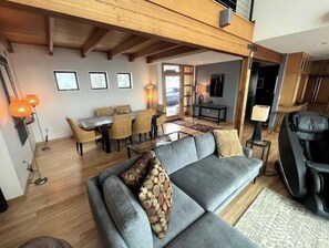 A spacious living area with a grey sofa, wooden flooring, and a dining area with a table and chairs.