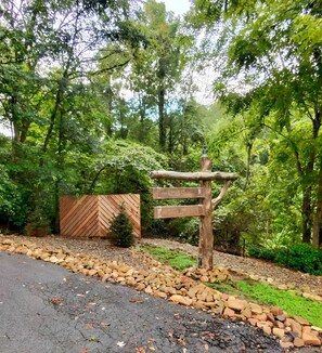 A rustic wooden signpost in a lush garden with a herringbone-patterned fence and a gravel path.