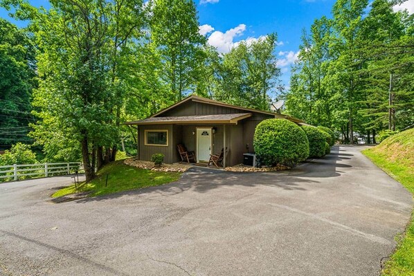 A small, single-story cabin with a front porch, a covered outdoor seating area, and a well-maintained lawn.