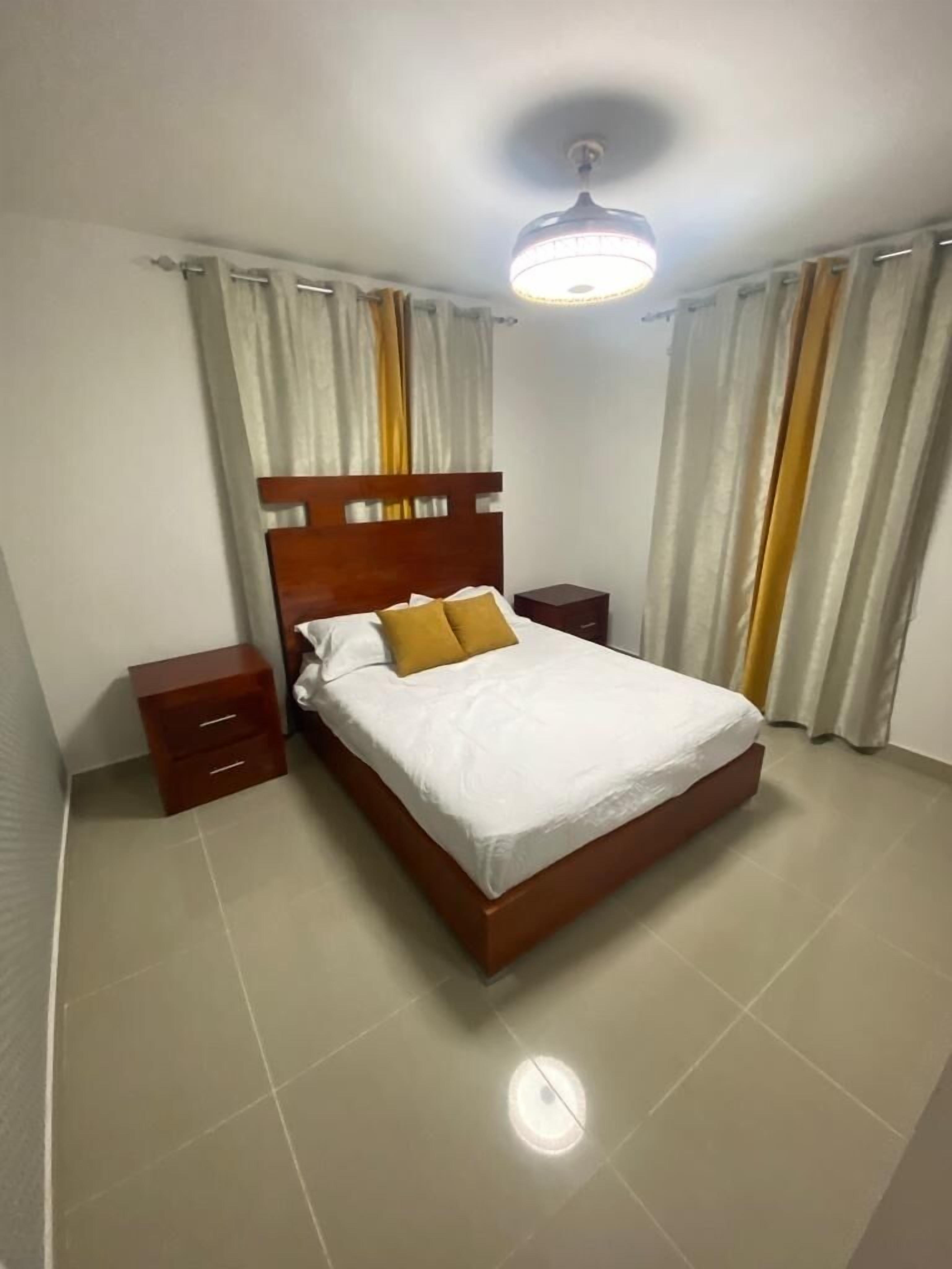 A bedroom with a wooden bed, two nightstands, a ceiling light, and curtains.