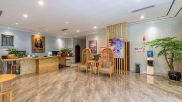 A hotel reception area with a wooden reception desk, several chairs, and a large painting on the wall.