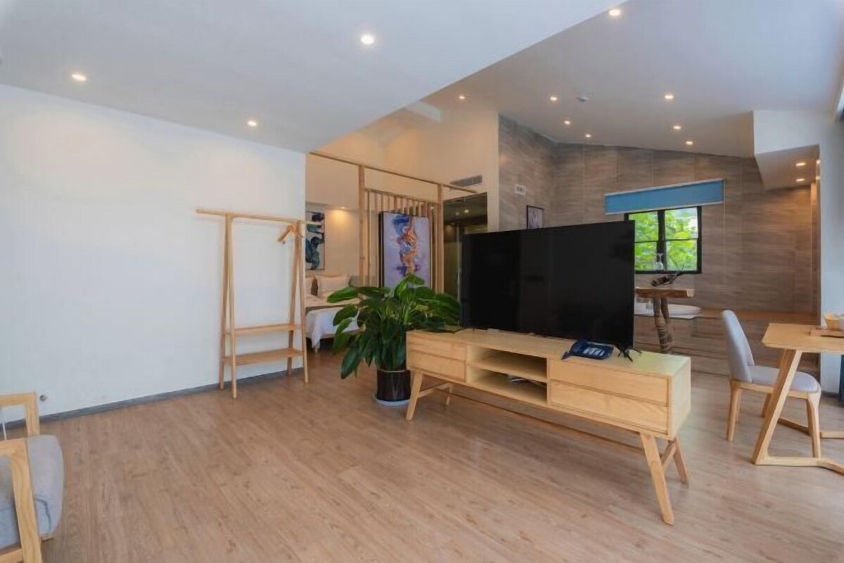 Uma sala de estar moderna com um móvel de entretenimento de madeira, uma TV de tela plana, uma planta em vaso e um espaço de jantar com mesa e cadeiras.