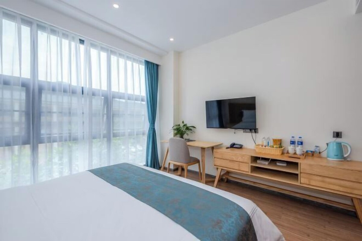 Quarto de hotel moderno com uma cama grande, uma mesa de escritório, televisão de tela plana e uma janela ampla com cortinas.