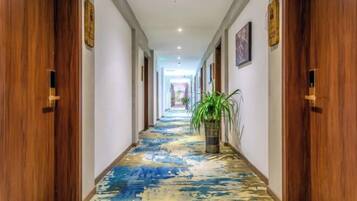 Un pasillo de hotel con puertas de madera, una alfombra estampada en azul y amarillo, y una planta en maceta.