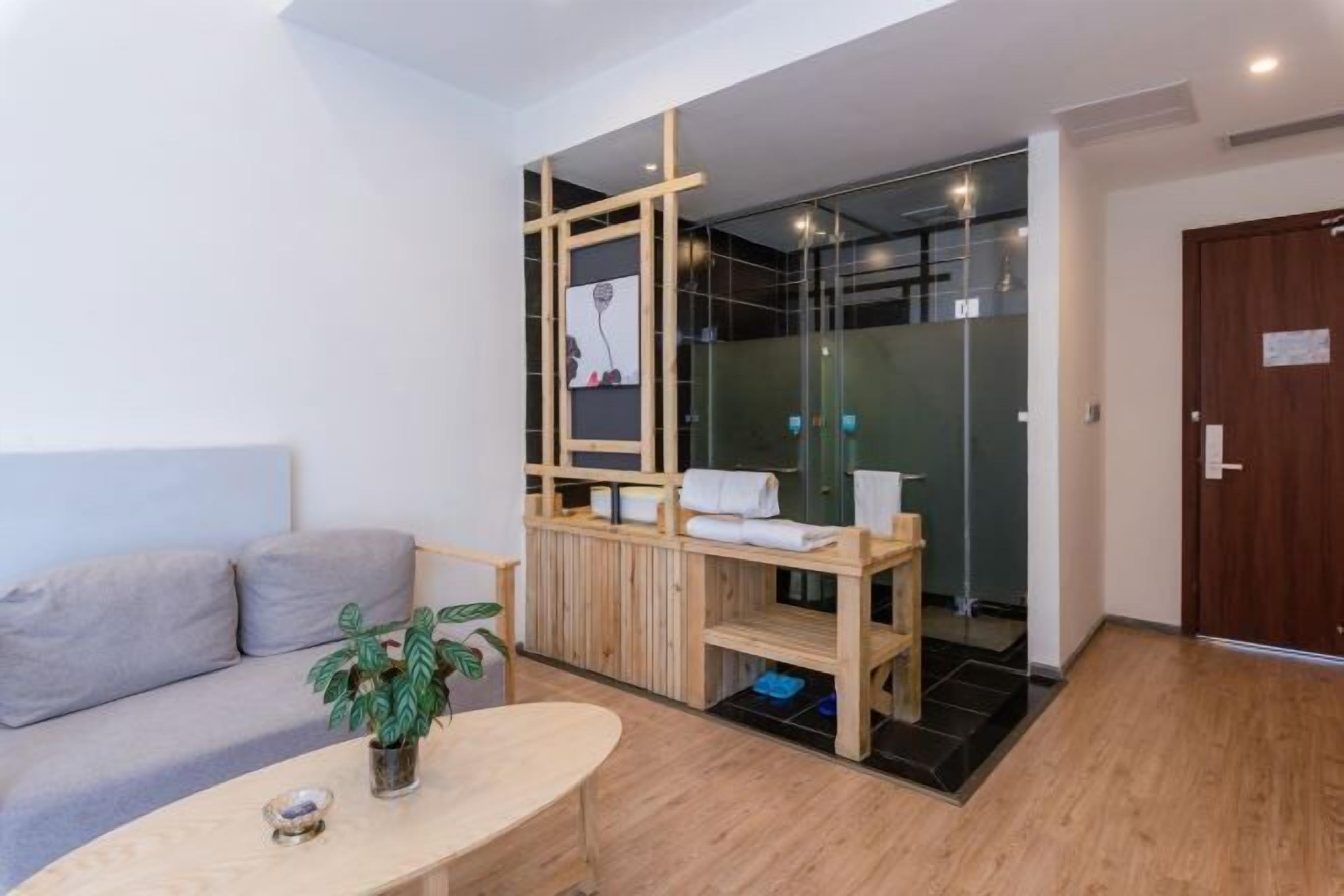 Habitación moderna con sofá, una mesita con una planta, un separador de madera y una zona de ducha de vidrio.