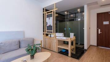 Habitación moderna con sofá, una mesita con una planta, un separador de madera y una zona de ducha de vidrio.