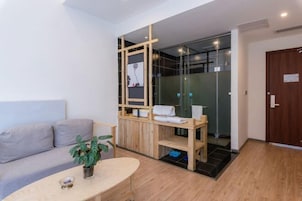 Habitación moderna con sofá, una mesita con una planta, un separador de madera y una zona de ducha de vidrio.
