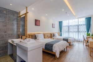 Una habitación de hotel moderna con dos camas, un baño con un espejo grande y vistas a la ciudad a través de amplios ventanales.