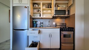 A compact kitchen with a stainless steel refrigerator, a microwave, an oven, and a sink.