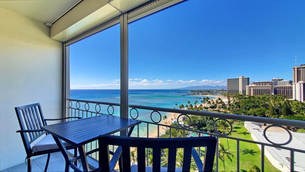 Un balcón con mesa y sillas, con vista a la playa y al paisaje urbano.