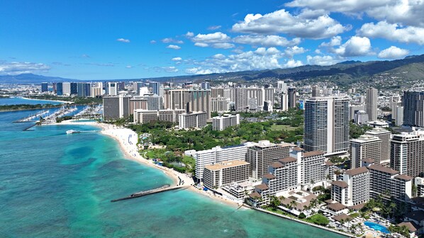 A coastal cityscape with high-rise buildings, a beach, and clear blue waters.