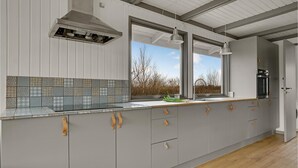 Una cocina moderna con gabinetes grises, salpicadero de azulejos y ventana con vistas a un paisaje natural.