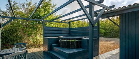 Una terraza de madera con un jacuzzi integrado, un banco y una estructura de pérgola.