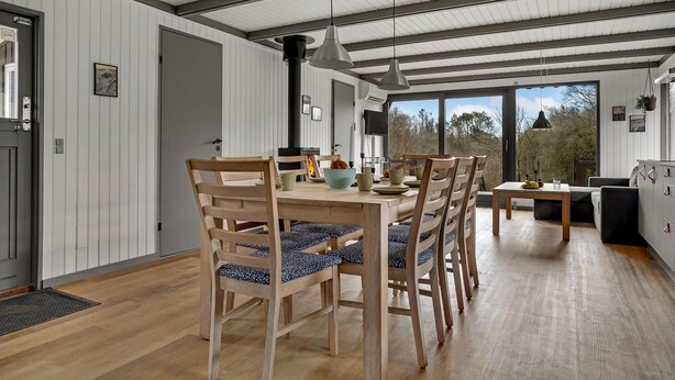 Un comedor con mesa y sillas de madera, una lámpara colgante moderna y vistas amplias a través de grandes ventanales.