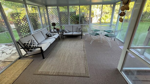 A sunroom with a gray sofa, two chairs, a small table, and a patterned rug.
