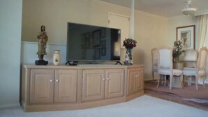 A living room with a flat-screen TV on a wooden cabinet, a statue, and a vase with flowers.