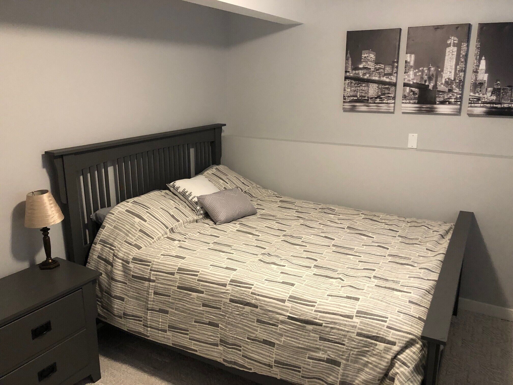 A bedroom with a bed, a nightstand, a lamp, and three black-and-white cityscape pictures on the wall.