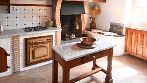 A rustic kitchen with exposed brick walls, a wooden ceiling, and a stone fireplace.