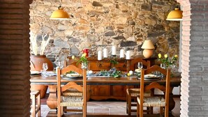 A dining area with a stone wall backdrop, a wooden table set for four, and hanging yellow lamps.