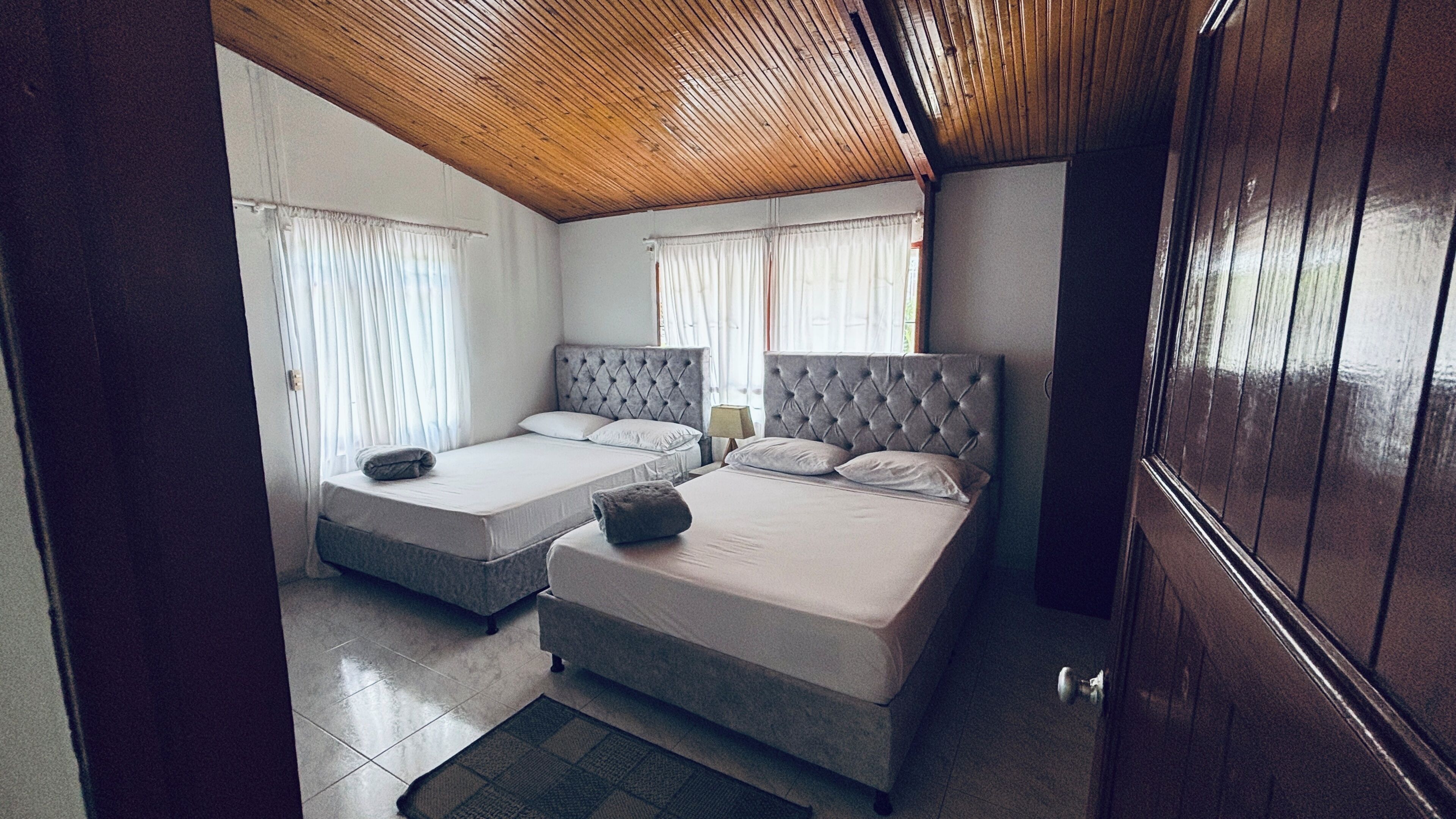 A room with two beds, a wooden ceiling, and a door.