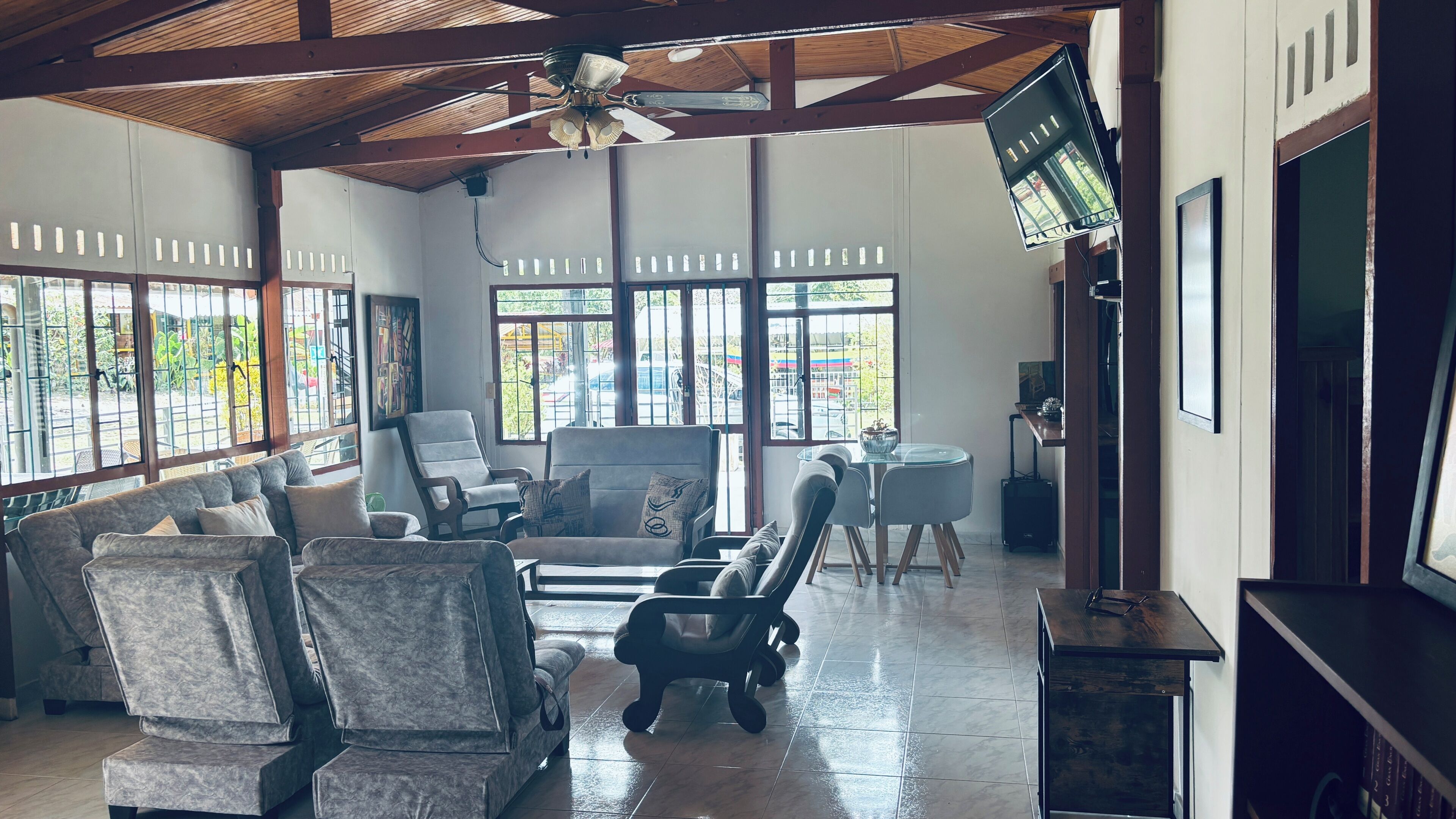 A spacious room with a high ceiling, large windows, and a ceiling fan. There are several chairs and a sofa arranged for seating.