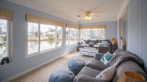 A spacious living room with a large window, a ceiling fan, and a gray sofa with blue and white cushions. - Waterfront Retreat w/ Hot Tub, Game Room, Kayaks, 2 Kings, + more! (White Stone)