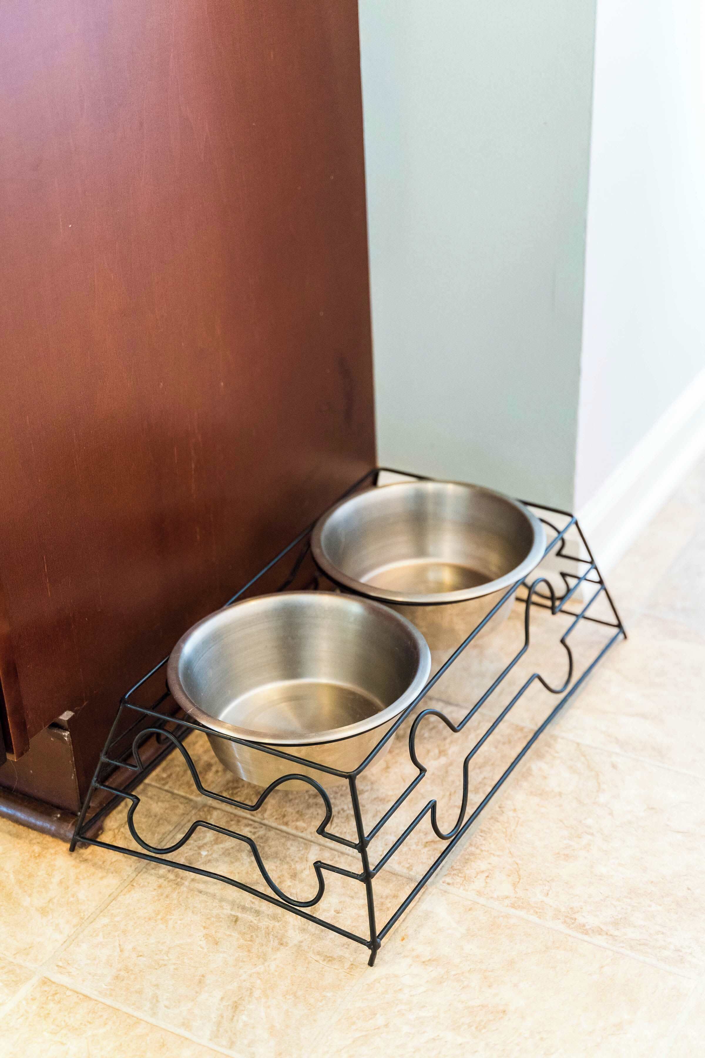 Un support métallique pour gamelle de chien, avec deux gamelles en acier inoxydable, posé sur un sol carrelé.