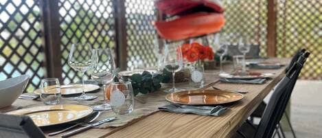 An outdoor dining area with a wooden table set for four, surrounded by chairs.