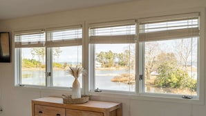 A room with three large windows, a wooden dresser, and a vase with dried plants. - Waterfront Retreat w/ Hot Tub, Game Room, Kayaks, 2 Kings, + more! (White Stone)