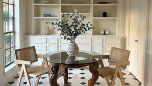 A dining area with a round glass table, two wooden chairs, a vase with flowers, and a ceiling light fixture. - Mr. Nomad: Artistic Abode in Uptown (Dallas)