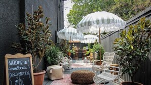 A cozy outdoor patio area with wicker chairs, a chalkboard sign, and striped umbrellas. - Mr. Nomad: Artistic Abode in Uptown (Dallas)