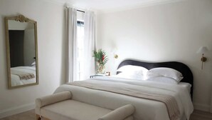A bedroom with a bed, a bench, a mirror, and a window with curtains. - Mr. Nomad: Artistic Abode in Uptown (Dallas)
