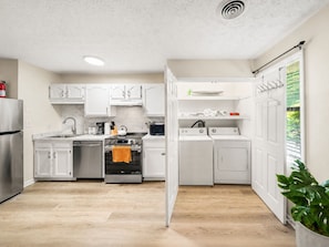 A modern kitchen with white cabinets, stainless steel appliances, and a wooden floor.